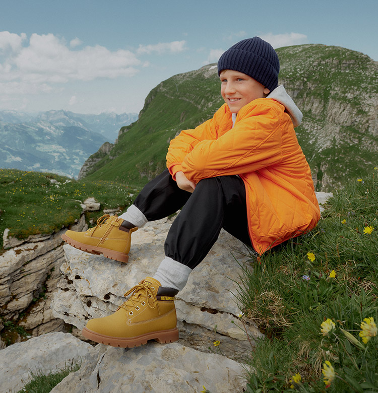 Kind in orangener Jacke sitzt auf einem Berg